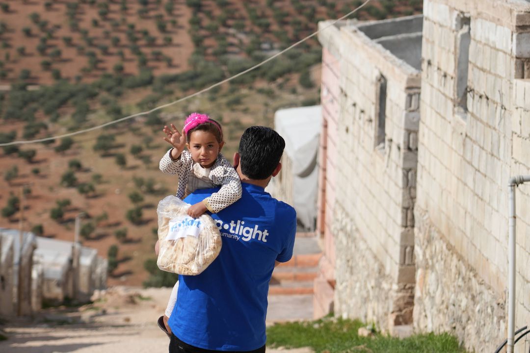 A Spotlight Charity volunteer carrying a child and a bag of bread